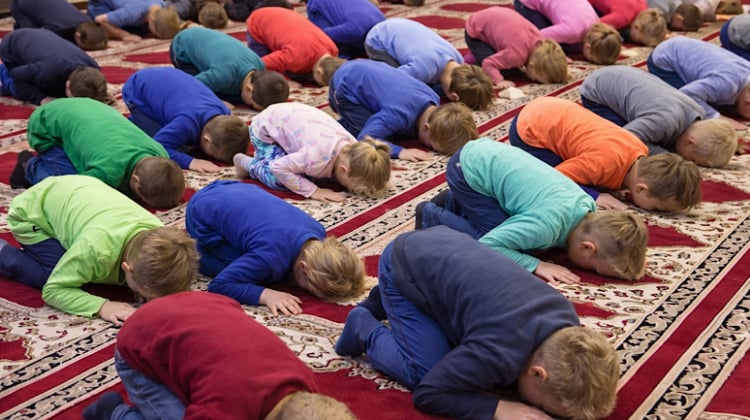 Children kneeling on prayer mats in a classroom during an Islamic prayer exercise at a Church of England primary school in Lincolnshire